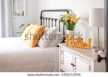 Cheerful yellow hello sign and fresh flowers in a clean and bright bedroom Royalty-Free Stock Photo #1906113904