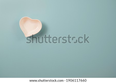 White small ceramic heart shape bowl on blue and copy space on blue background for valentines’s day concept.