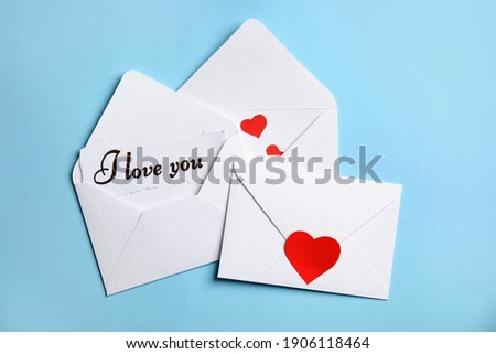 Card with phrase I Love You in envelope and red hearts on light blue background, flat lay