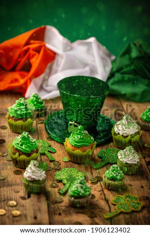 Happy St Patricks Day leprechaun hat with cupcakes and Irish flag on vintage style wood background