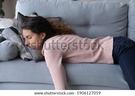 Tired unmotivated young woman falls asleep on cozy couch indoors, having no energy after hard working day. Exhausted caucasian lady napping on comfortable sofa in living room, fatigue concept. Royalty-Free Stock Photo #1906127059