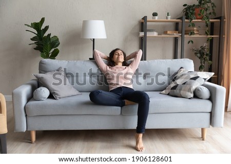 Full length peaceful happy young woman relaxing on comfortable sofa, breathing fresh air, enjoying mindful lazy moment indoors. Smiling millennial caucasian lady meditating alone in living room. Royalty-Free Stock Photo #1906128601