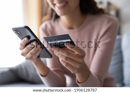 Close up smiling millennial woman holding smartphone and banking credit card, involved in online mobile shopping at home, happy female shopper purchasing goods or services in internet store. Royalty-Free Stock Photo #1906128787