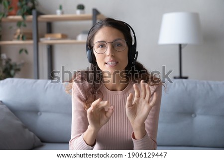 Web camera view smart young caucasian woman in eyeglasses wearing headset with microphone, holding distant negotiations meeting with colleagues from home or giving educational online lecture. Royalty-Free Stock Photo #1906129447