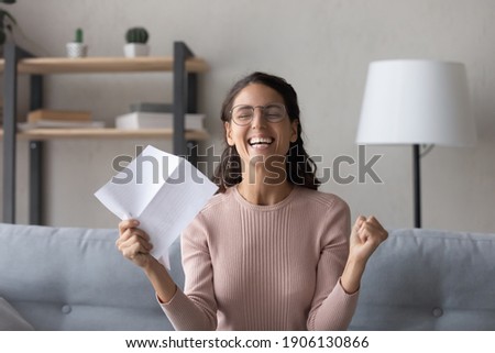 Emotional joyful millennial woman in glasses holding paper sheet in hands, getting dream job offer or university admission letter, celebrating professional success, reading loan approval notification. Royalty-Free Stock Photo #1906130866