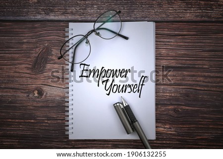 Selective focus image of spectacles and pen with Empower Yourself wording on a wooden background. Business and motivational concept