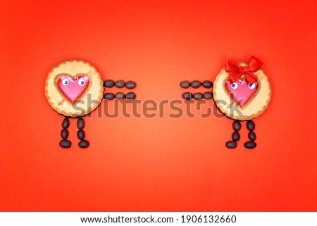 Two characters made of round cookies decorated with red jelly hearts and coffee beans trying to reach each other. Creative flat lay isolated on red background. Valentine's Day love concept.