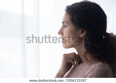 Head shot side view thoughtful young caucasian woman standing near window, looking in distance, thinking of difficult personal problems solutions, felling melancholic alone indoors, copy space. Royalty-Free Stock Photo #1906133587