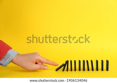 Woman causing chain reaction by pushing domino tile on yellow background, closeup. Space for text Royalty-Free Stock Photo #1906134046