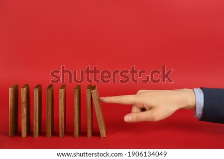 Woman causing chain reaction by pushing domino tile on red background, closeup. Space for text Royalty-Free Stock Photo #1906134049