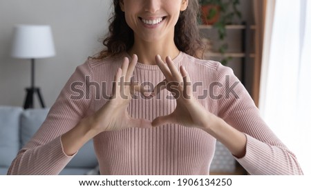 Close up cropped image smiling young woman showing heart love sign with fingers, feeling grateful indoors. Sincere happy millennial female volunteer expressing support and kindness, charity concept. Royalty-Free Stock Photo #1906134250