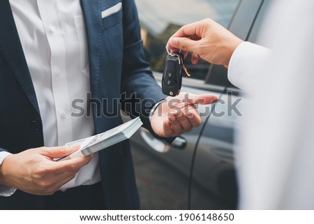 Closeup hand giving a car key and money for loan credit financial, lease and rental concept