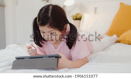 Young Asian girl drawing at home. Asia japanese woman child kid relax rest fun happy using tablet draw cartoon before sleep lying on bed, feel comfort and calm in bedroom at night concept.