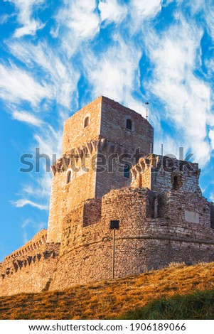 Close up view of medieval castle up the hill of Assisi, province in Umbria Italy. Stone bricks tower and walls at evening with clear clouds sky 