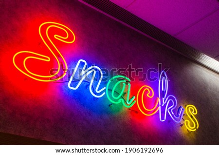 A neon sign that says the word Snacks in cursive multicolor letters