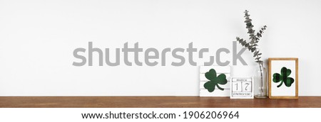 St Patricks Day decor on a wood shelf. Shabby chic wood signs, calendar and green branches against a white wall banner. Copy space.