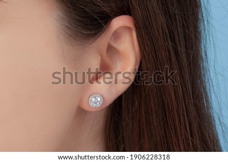 Round silver earrings on the ear of a well-groomed lady on a blue background Royalty-Free Stock Photo #1906228318