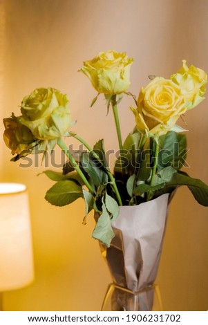 Five yellow roses in craft paper on a orange background with green leaves. Vertical image.