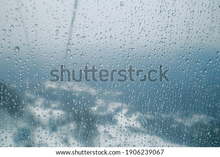 Rain drops on the scratches glass background. Snowed mountains, fog and blue cloudy sky behind.