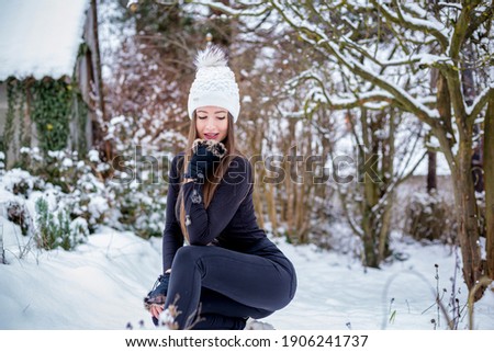 A beautiful smiling girl in black clothes and a white knitted hat in winter