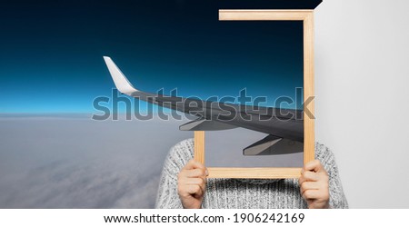 Artwork collage concept. Man holding a picture in frame on face; view of an airplane wing in the sky. Focus on wing.