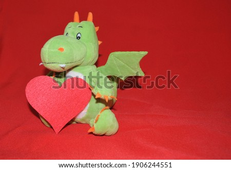 Plush green dinosaur with a heart in its paws on a red satin background.