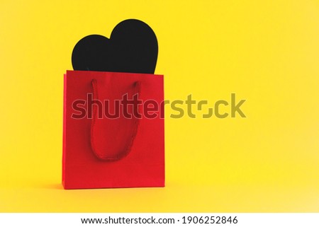 black heart shape in red packaging on yellow background, gift for valentine's day. Selective focus.