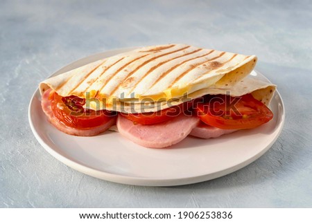 Tortillas with various fillings of ham, cheese, fried eggs on both sides and tomatoes. Food trend. Delicious sandwich for a snack or a full lunch or dinner. Royalty-Free Stock Photo #1906253836