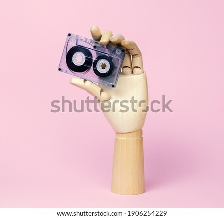 Wooden hand holding retro audio tape pastel pink background. Vintage music poster.