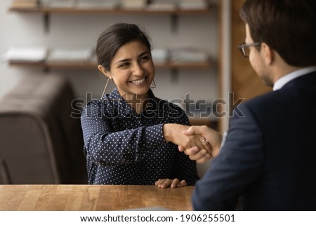Greetings, you are hired. Happy young indian female successful job seeker shake hand of male hr manager being accepted on vacant place. Diverse business partners handshake close deal come to agreement Royalty-Free Stock Photo #1906255501