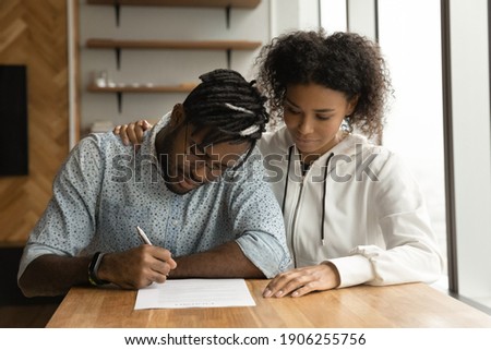 Focused young black couple signing prenuptial agreement in lawyer office. Concentrated millennial afro husband wife insuring life property read paper document before write names and certify contract