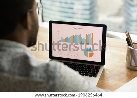 Black man sales manager financial analyst thinking on statistical information comparing data in charts graphs accessing marketing strategy effectiveness. Over shoulder view on laptop screen. Close up