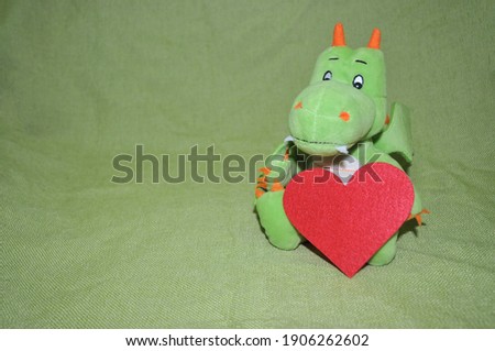 plush green dinosaur with a heart in its paws on a green background