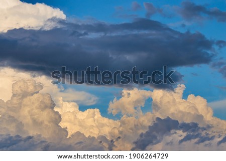 dark cloud floating over white cumulus clouds slightly shaded with yellow under a heavenly blue sky.