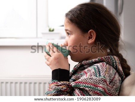 Little girl with dark hair drinking tea at home