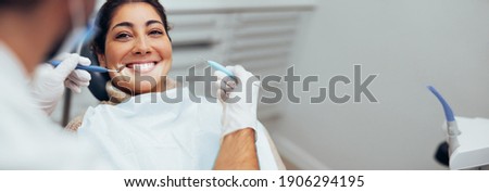 Dentist examining teeth of a female patient in dental clinic using dental tools. Happy woman getting dental treatment. Royalty-Free Stock Photo #1906294195