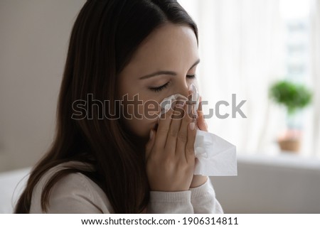 Close up of unhealthy young Caucasian woman blow in napkin suffer from flu or cold. Unwell sick millennial female snuffle struggle with virus symptoms, have runny nose. Corona, covid-19 concept. Royalty-Free Stock Photo #1906314811