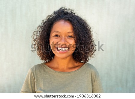 Close up horizontal portrait smiling young African American woman with curly hair against green background