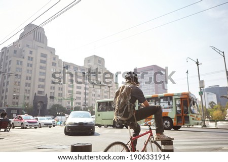 young cyclist waiting to cross a main avenue in downtown Mexico City, in the background a public transport bus can be seen.