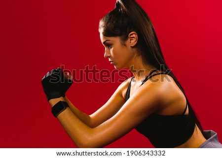 A sporty girl with long hair looks seriously to the side during physical exercises. Profile photo on a red background.