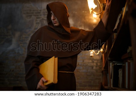 Male exorcist in black hood holding a torch