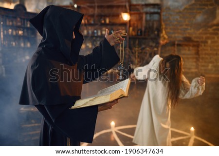 Exorcist in hood casting out demons from a woman Royalty-Free Stock Photo #1906347634
