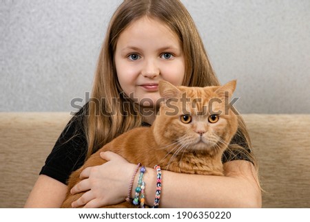Attractive little girl with red fluffy cat on a sofa in a room. Focus on the girl.