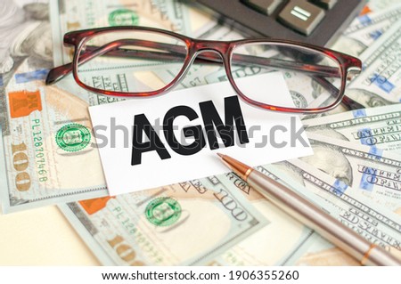 Finance and business concept. On the table are bills, glasses, pen and a sign on which it is written - AGM.