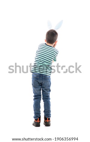 Back view of amazed fascinated young boy with Easter bunny ears watching away with head in hands. Full length isolated on white background.