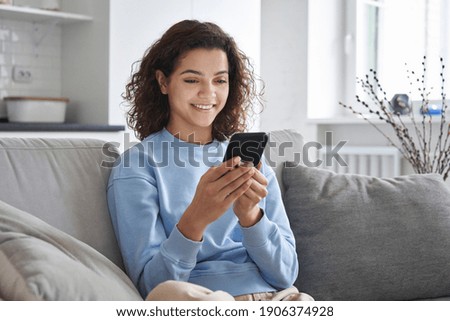 Happy hispanic teen girl holding cell phone using smartphone device at home. Smiling young latin woman blogger subscribing new social media, buying in internet, ordering products online in apps. Royalty-Free Stock Photo #1906374928
