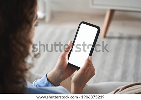 Young woman or teen girl hands holding smart phone with mockup white blank display, empty screen for social media app ads at home. Mobile applications technology concept, over shoulder close up view.