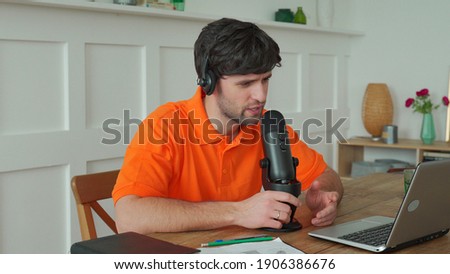 Man is speaking in microphone in studio recording podcast gesturing expressing opinions for online blog.