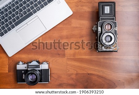 An old 35mm reflex camera, and an old medium format twin lens reflex camera, seen from above with a modern laptop next to them, horizontal