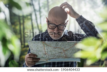 Middle aged man exploring a forest, he is lost and holding a map Royalty-Free Stock Photo #1906404433